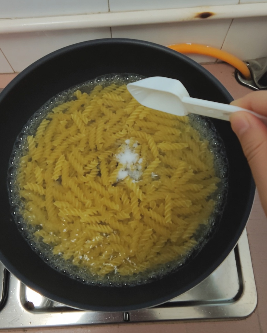 Un cucchiaio di sale aggiunto alla pentola con la pasta in cottura.
