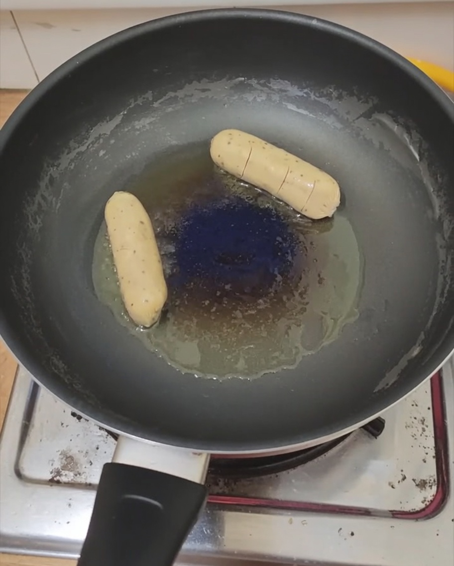 Un uovo al tegamino e una salsiccia che cuociono in padella.