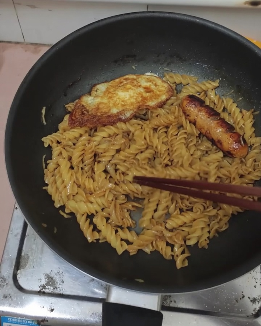 Uovo e salsiccia serviti sopra i fusilli al pepe nero in padella.