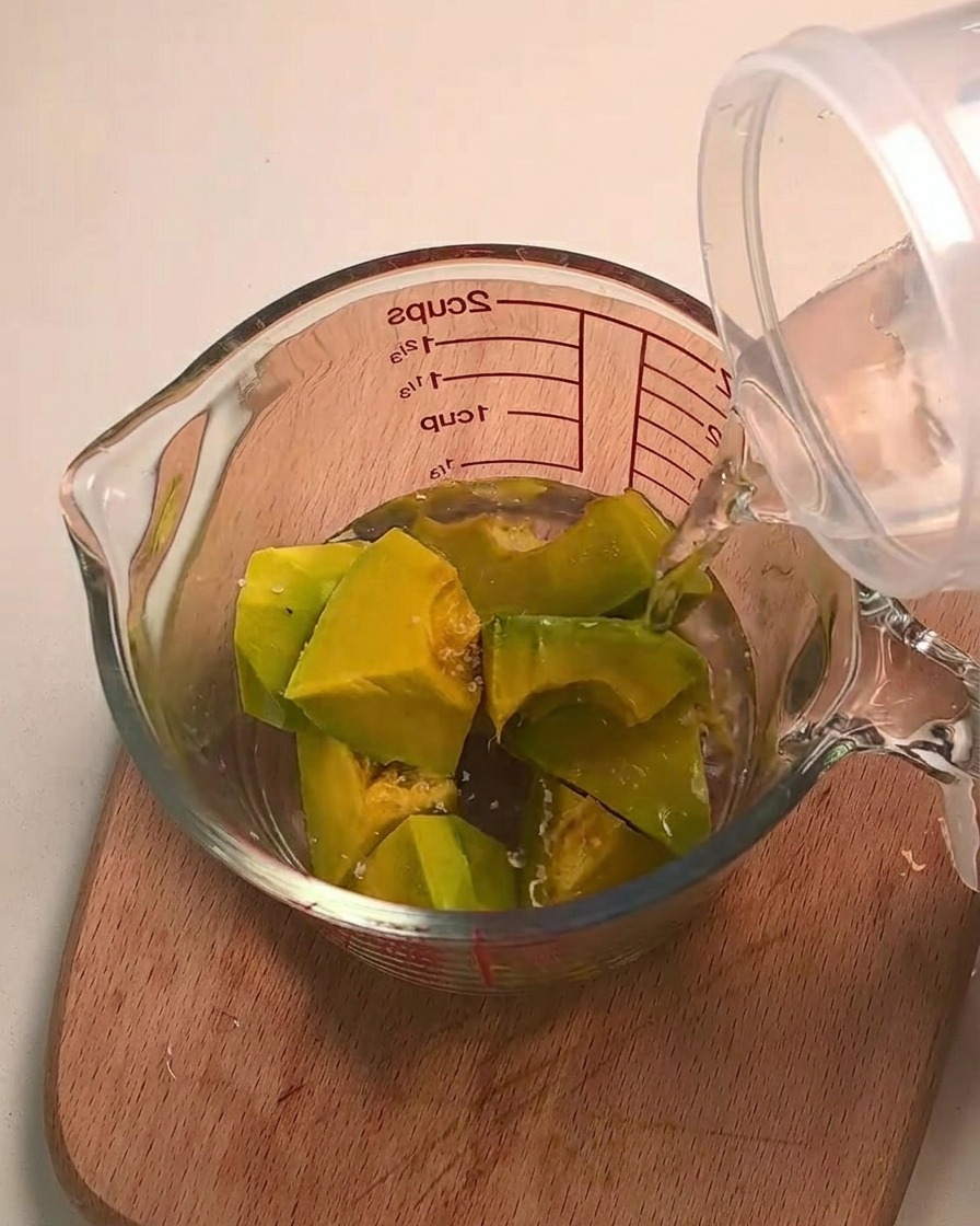 Acqua versata sui cubetti di zucca kabocha in una caraffa di vetro dosatrice.