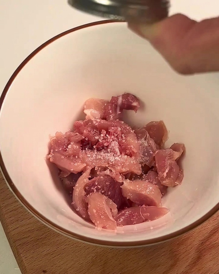 Pezzetti di coscia di pollo conditi con sale e succo di limone in una ciotola bianca.