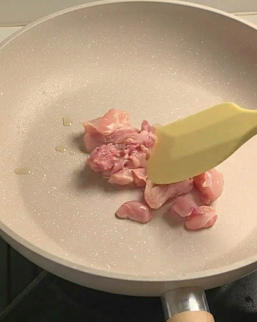 Pezzetti di pollo in cottura saltati in una padella antiaderente, leggermente dorati.