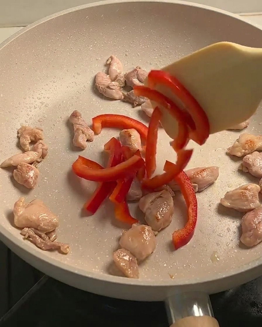Pollo saltato, peperoni rossi affettati e funghi cotti insieme in una padella.