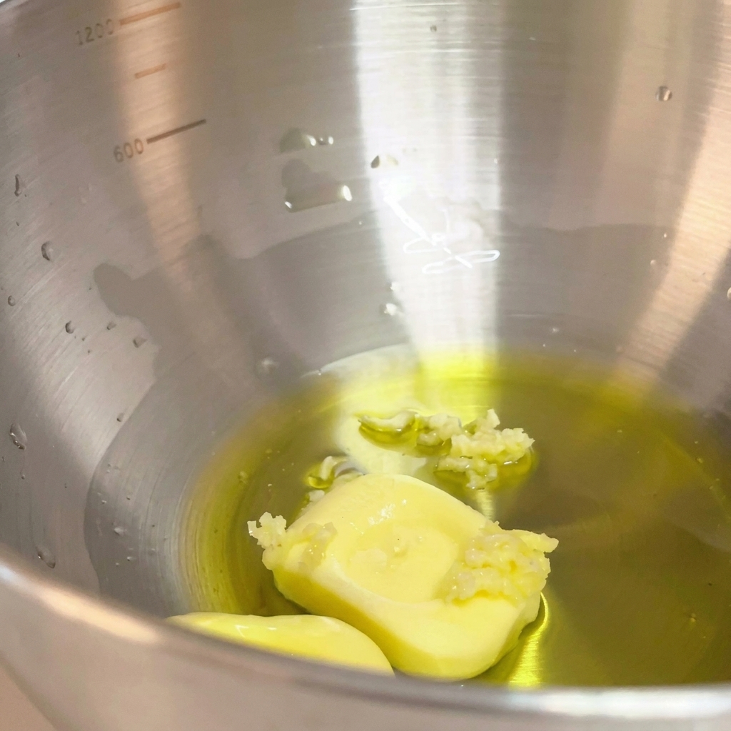 Aglio schiacciato aggiunto alla miscela di olio doliva e burro nella ciotola di metallo.