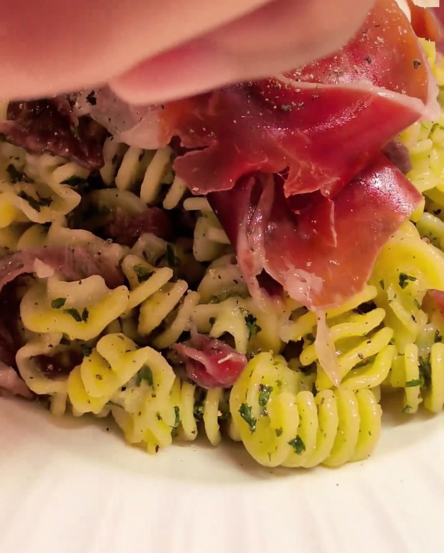 Fusilli mantecati in una ciotola con la salsa usando delle pinze da cucina.