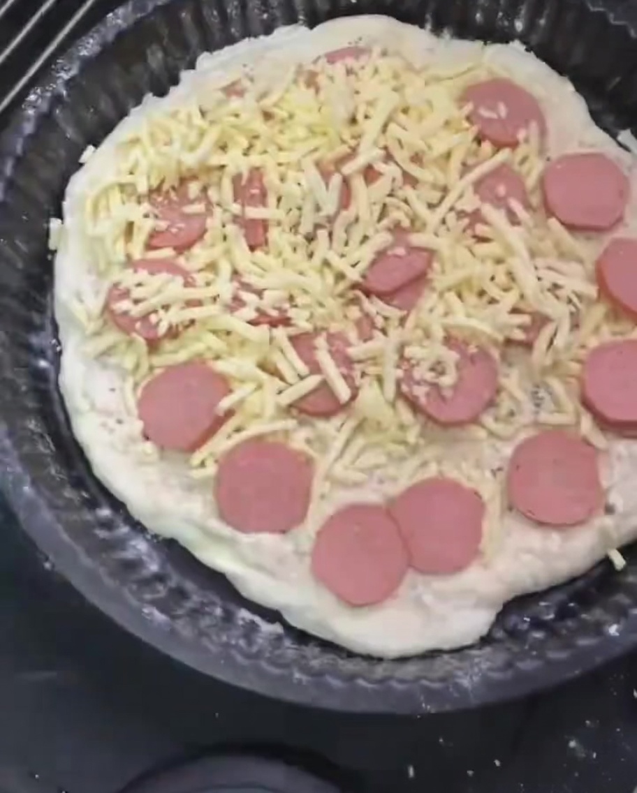 Un ultimo strato di mozzarella sparsa sopra la pizza condita.