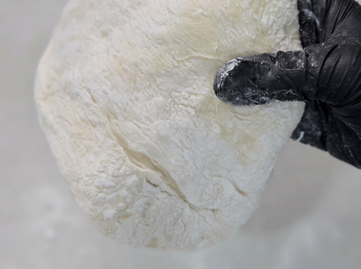 Impasto per pizza steso su una superficie infarinata con farina di mais.