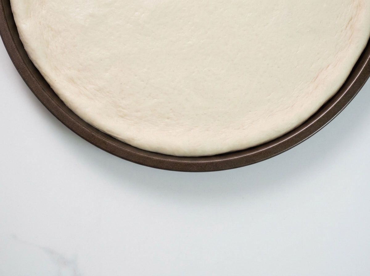 Un cucchiaio che spalma la salsa al tartufo nero sulla base cruda della pizza.
