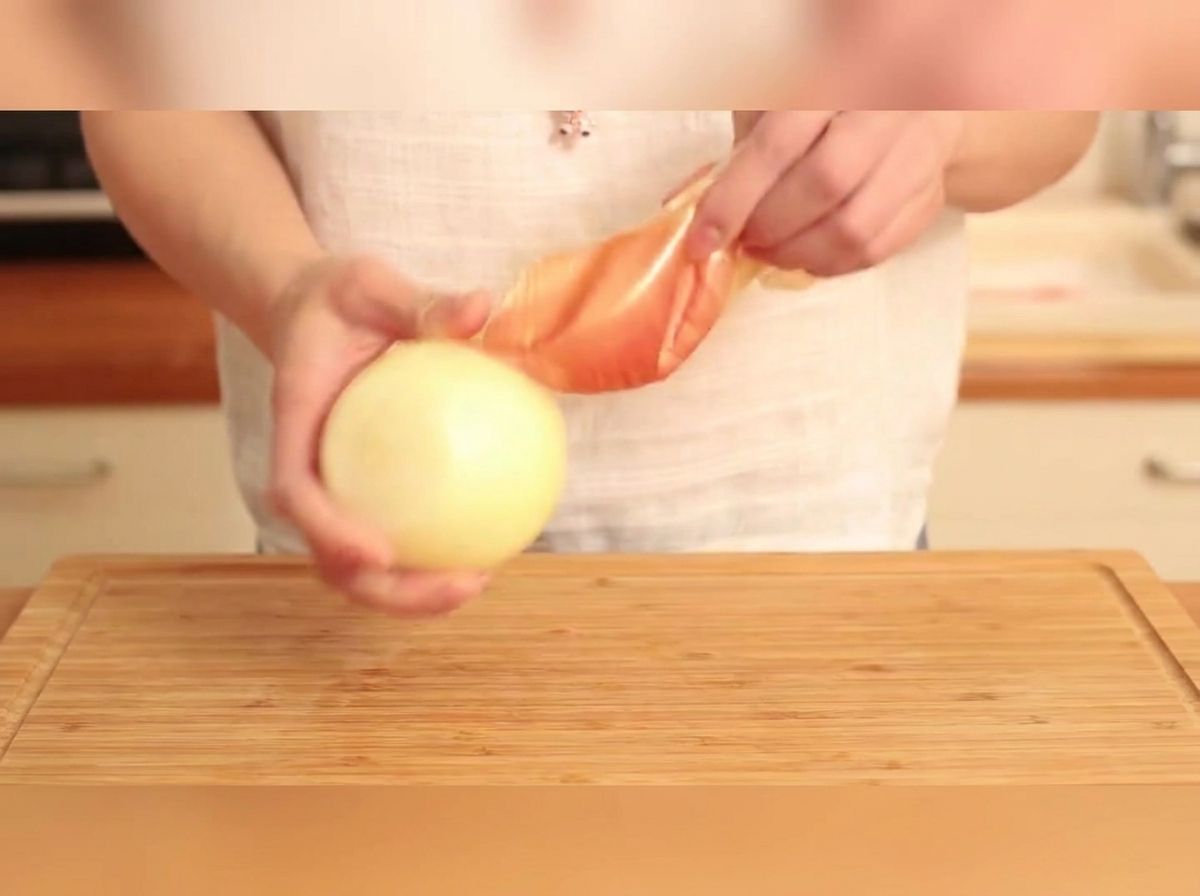 Una cipolla dorata sbucciata che viene tagliata a strisce su un tagliere di legno.