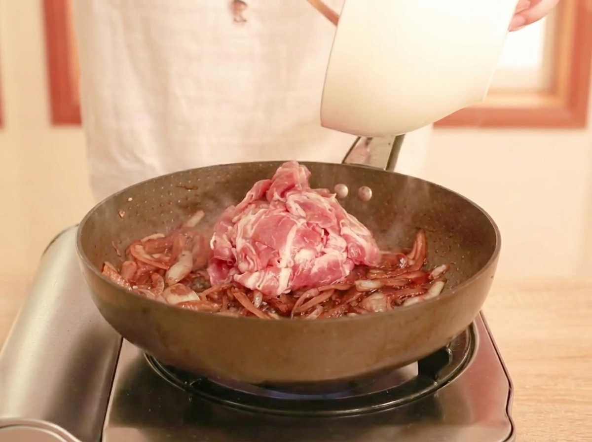 Manzo crudo affettato aggiunto in padella con salsa scura e cipolle, pronto per essere saltato.