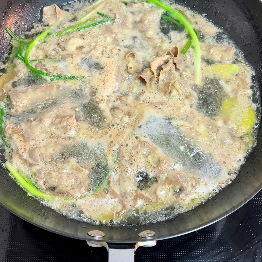 Fette di manzo e cipollotti freschi sbollentati in una padella di acqua bollente.