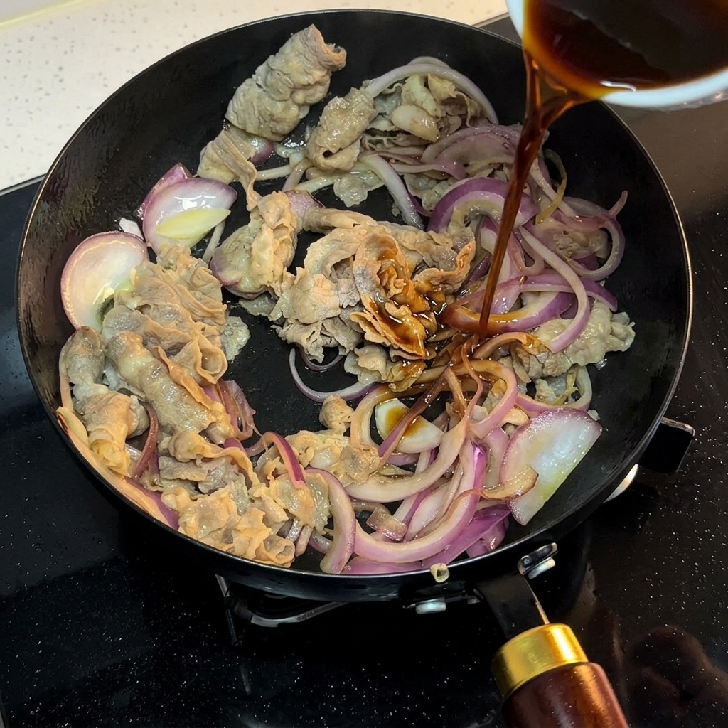 Una salsa scura versata da una piccola ciotola in una padella con manzo e cipolle.