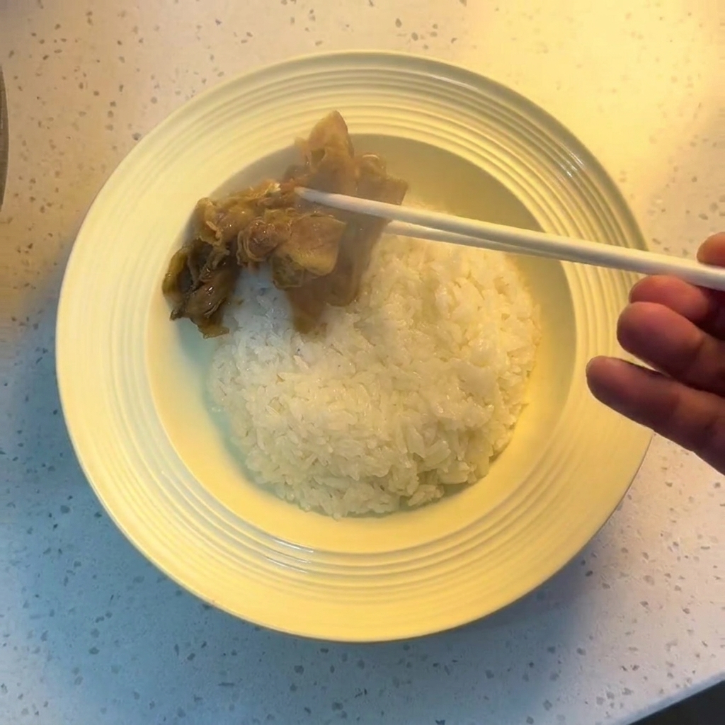 Bacchette che dispongono manzo e cipolle cotte sopra una ciotola di riso bianco.