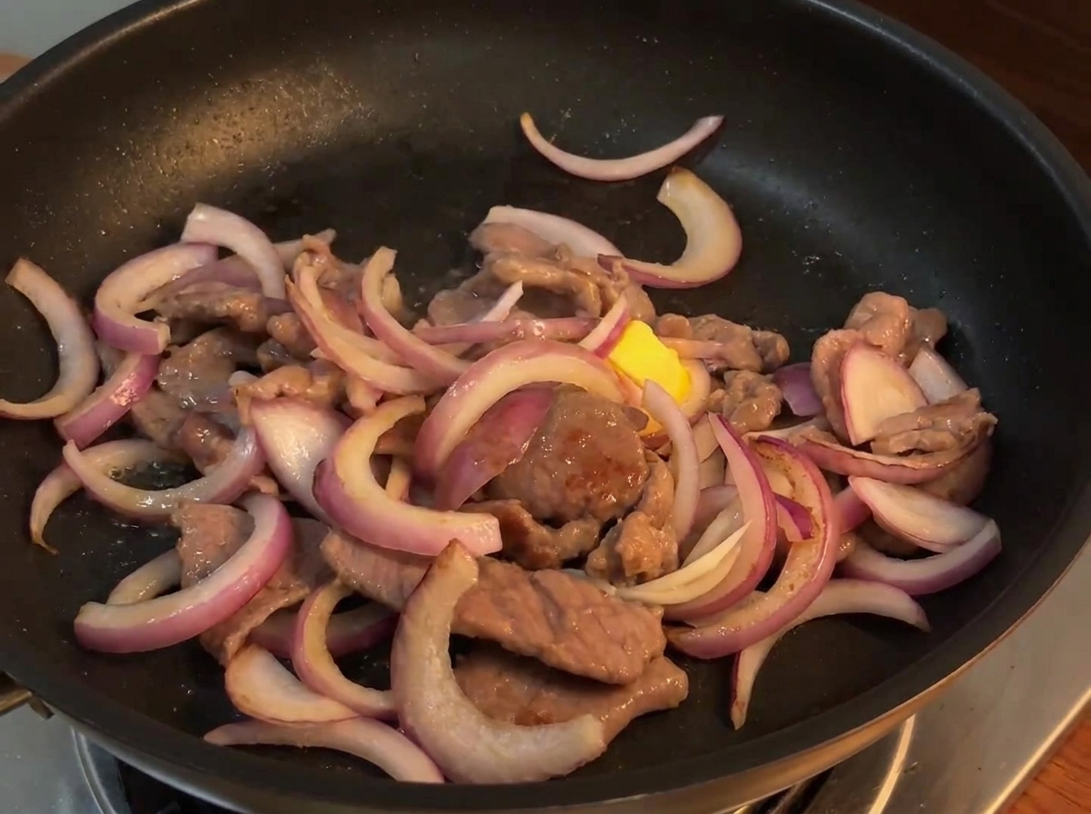 La salsa per il soffritto versata da una piccola ciotola sul mix di manzo e cipolla in una padella calda.