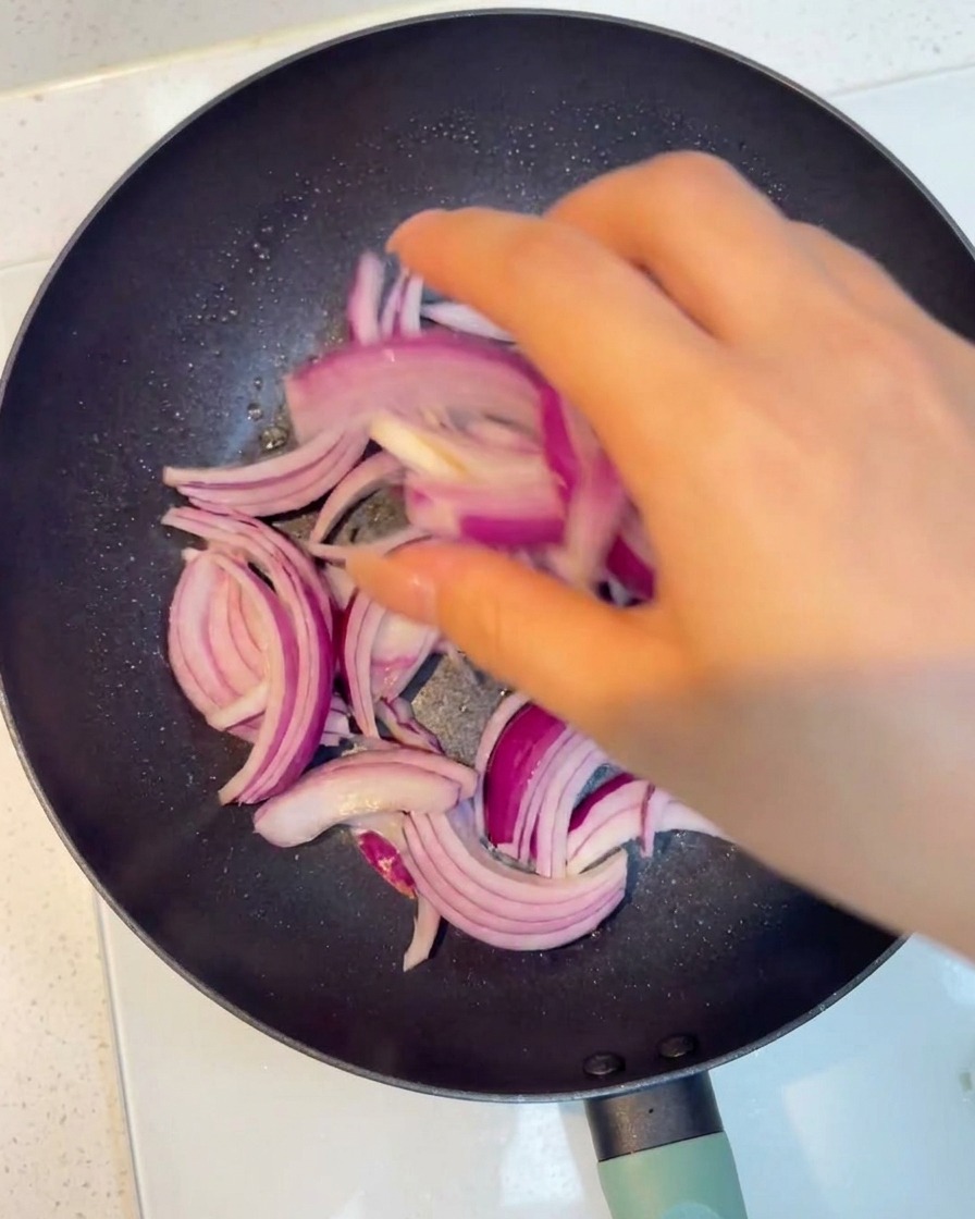 Fette di cipolla rossa che appassiscono in una padella calda.