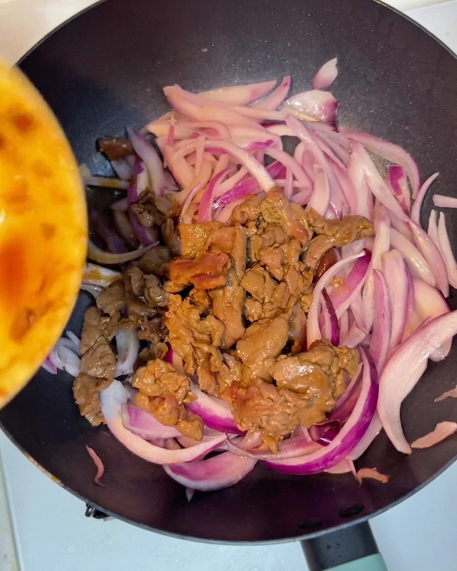 Manzo cotto aggiunto in padella insieme alle cipolle per essere mescolato.