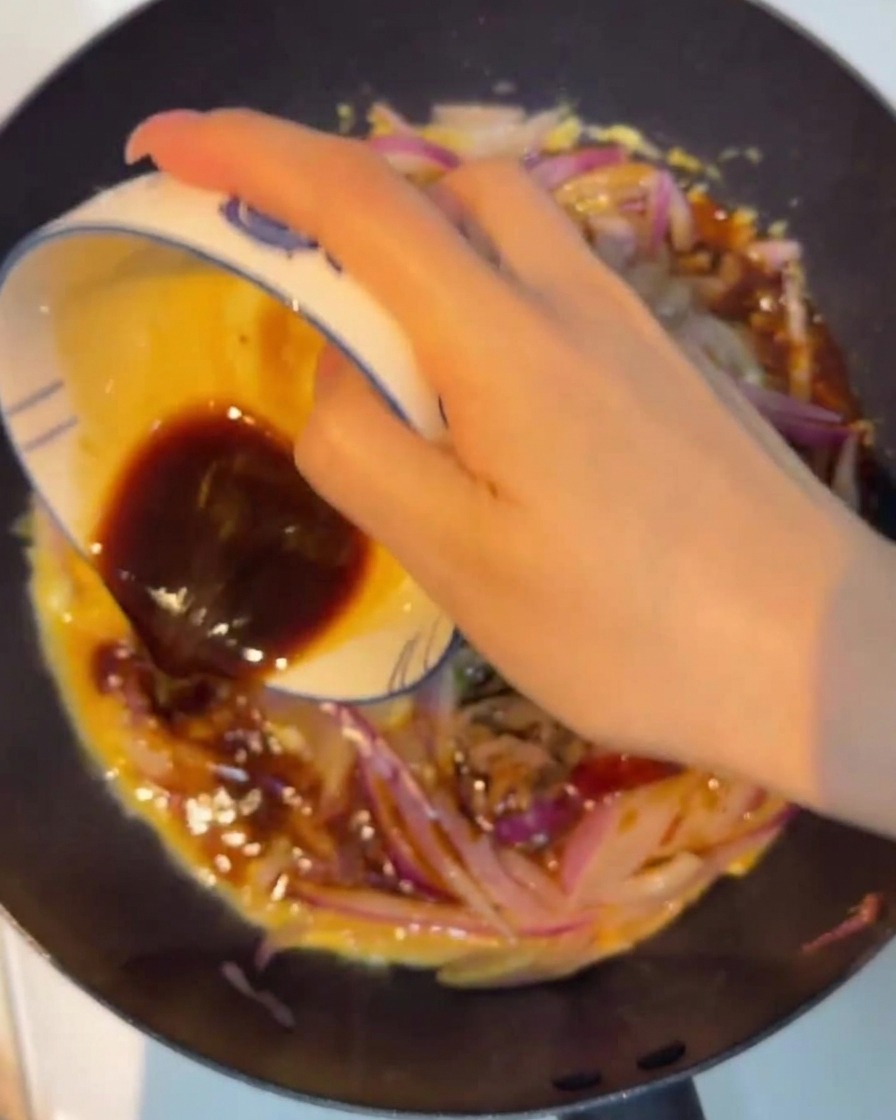 Salsa scura versata su manzo, cipolle e uova in una padella antiaderente.