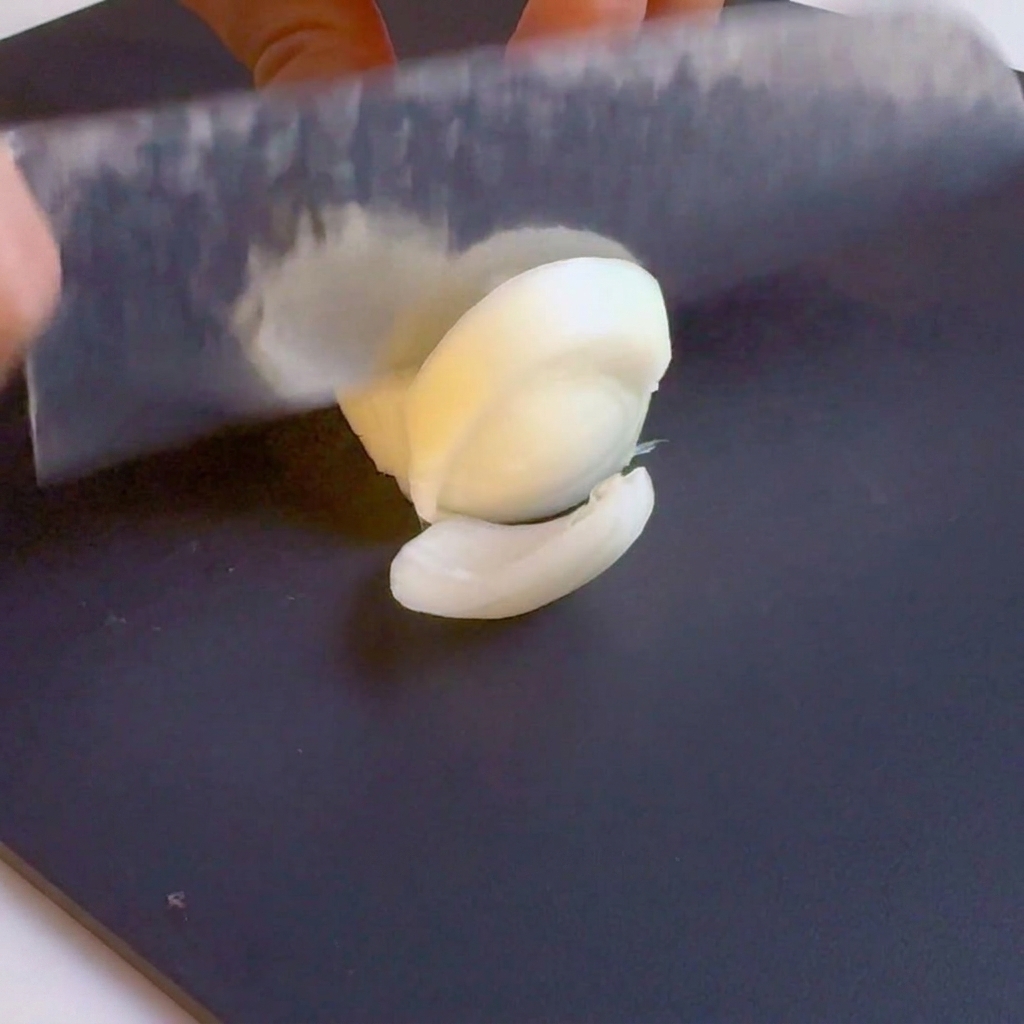 Un coltello affetta una cipolla bianca a listarelle su un tagliere nero.