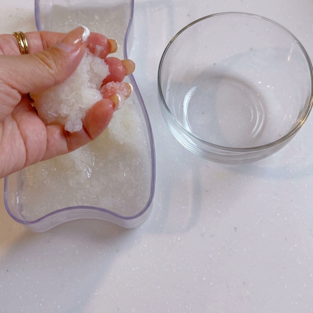Una mano strizza lacqua dal daikon grattugiato accanto a una ciotola di vetro trasparente.