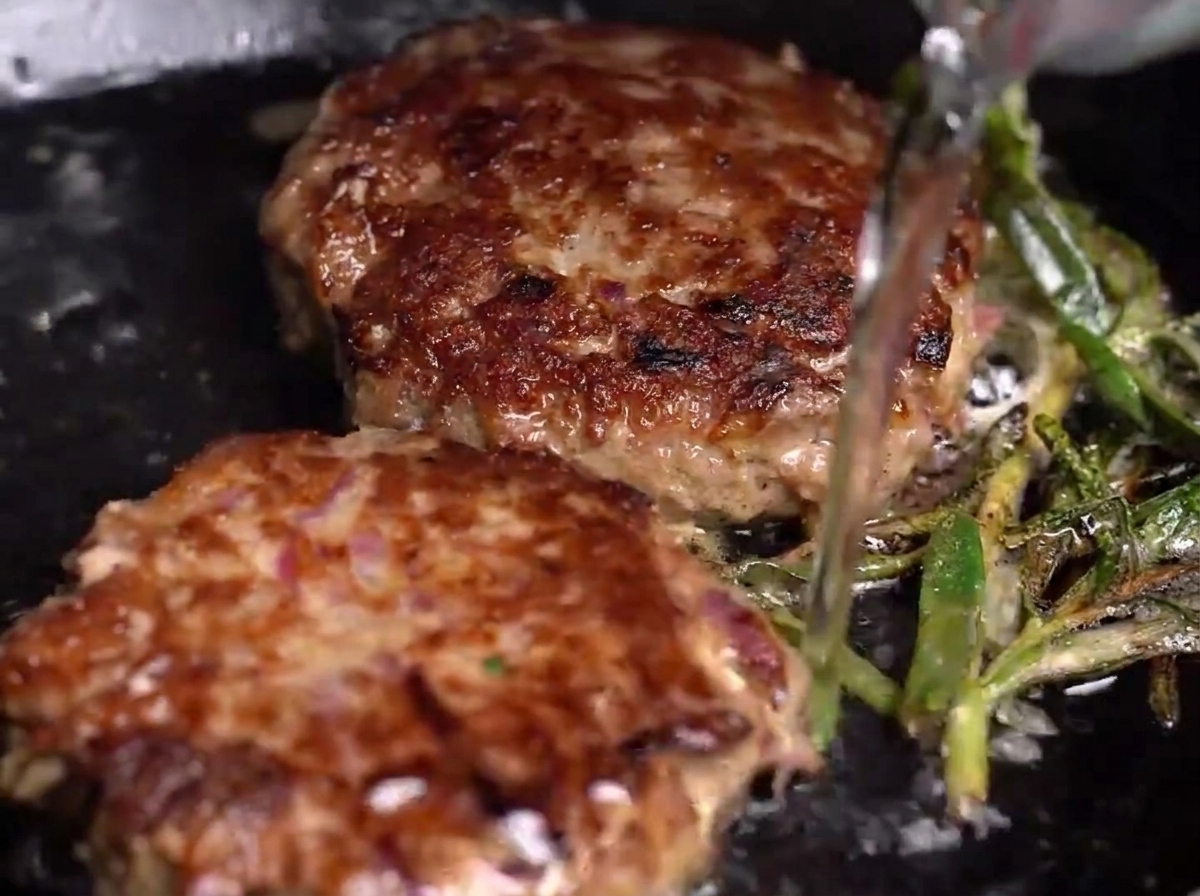 Acqua versata in una padella calda con hamburger e erbe, creando vapore.