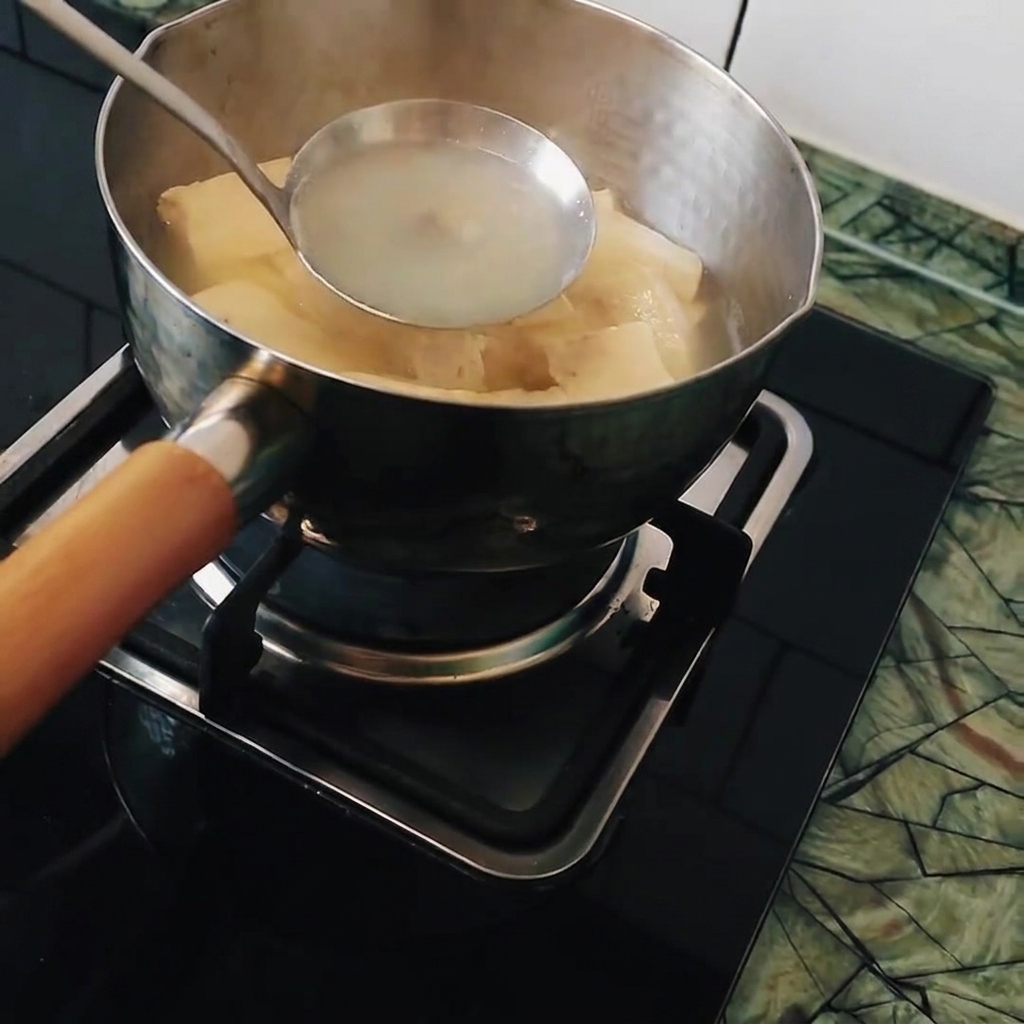 Un mestolo che mescola una pentola di acqua calda e tofu, preparandosi a sciogliere i blocchi di curry giapponese.