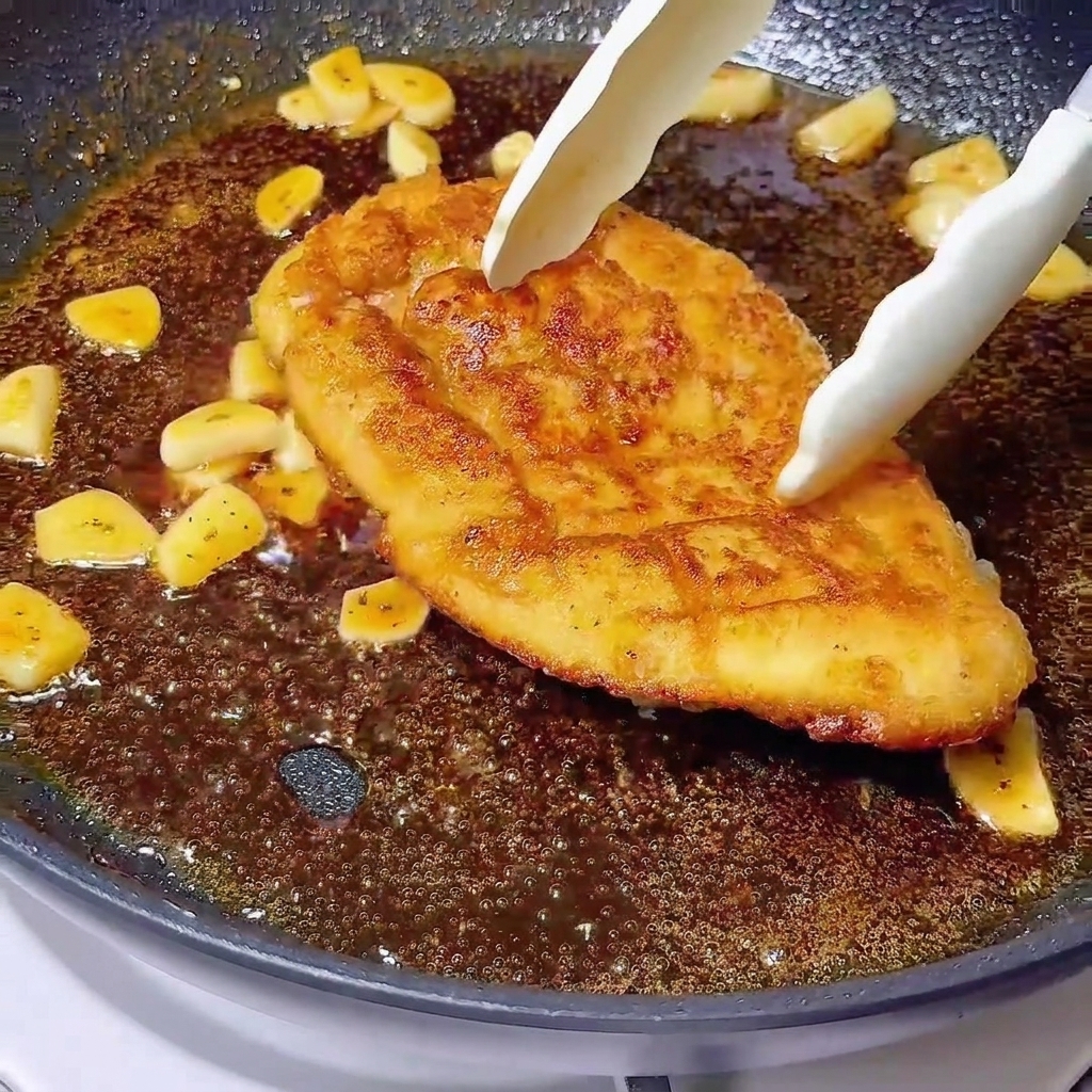 Pinze che ripongono un petto di pollo dorato in una glassa scura bollente con aglio a fette.