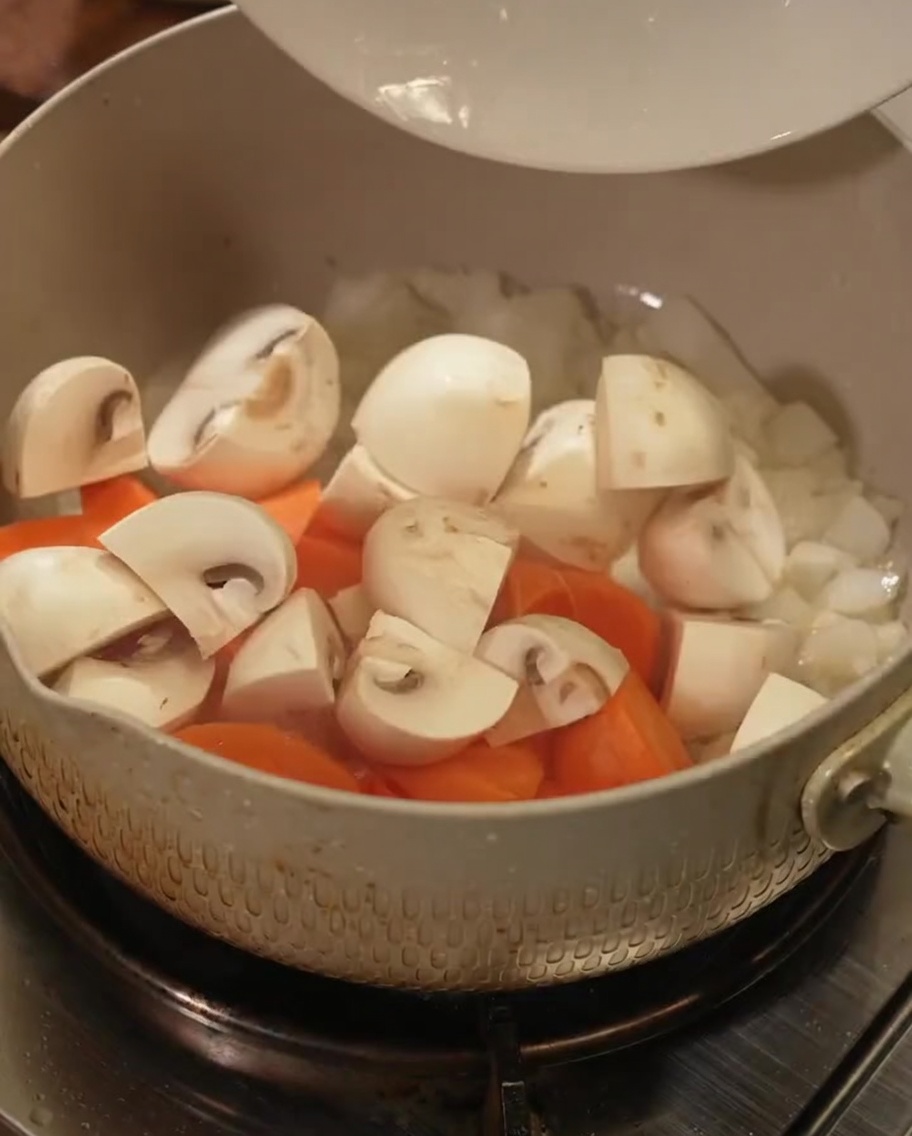 Pezzi di carota fresca e funghi affettati versati in una pentola.
