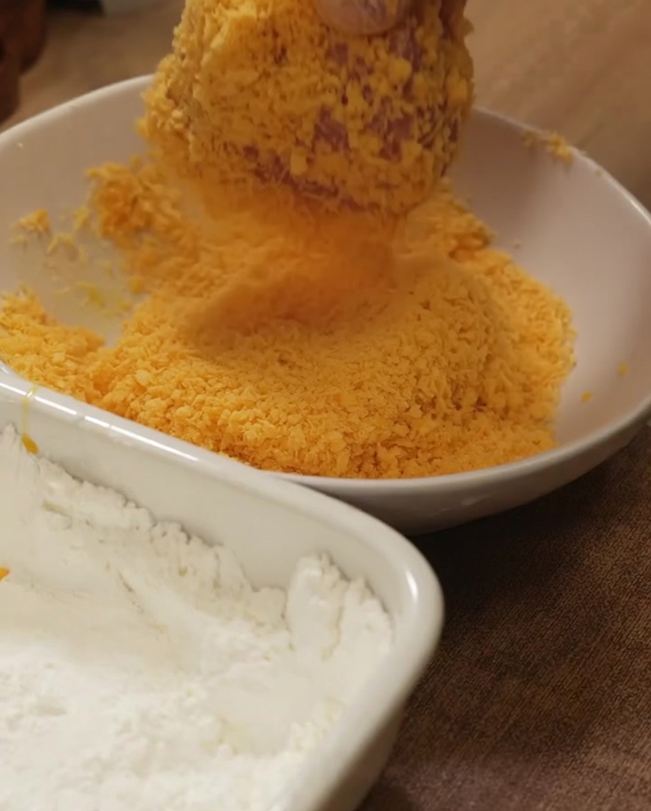 Petto di pollo pressato nel pangrattato dorato per una copertura uniforme.