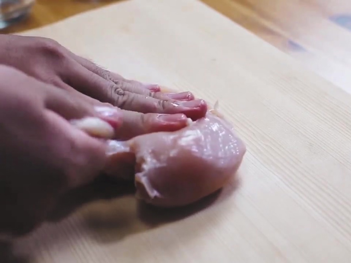 Un petto di pollo crudo viene cosparso di sale su un tagliere di legno.