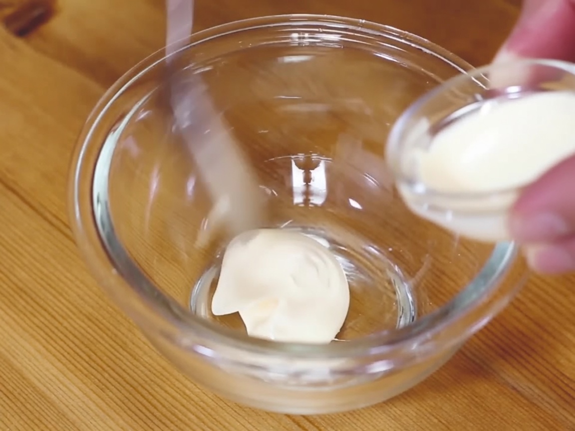 Una piccola ciotola di vetro contenente un composto cremoso di maionese e wasabi, mescolato con un cucchiaio.