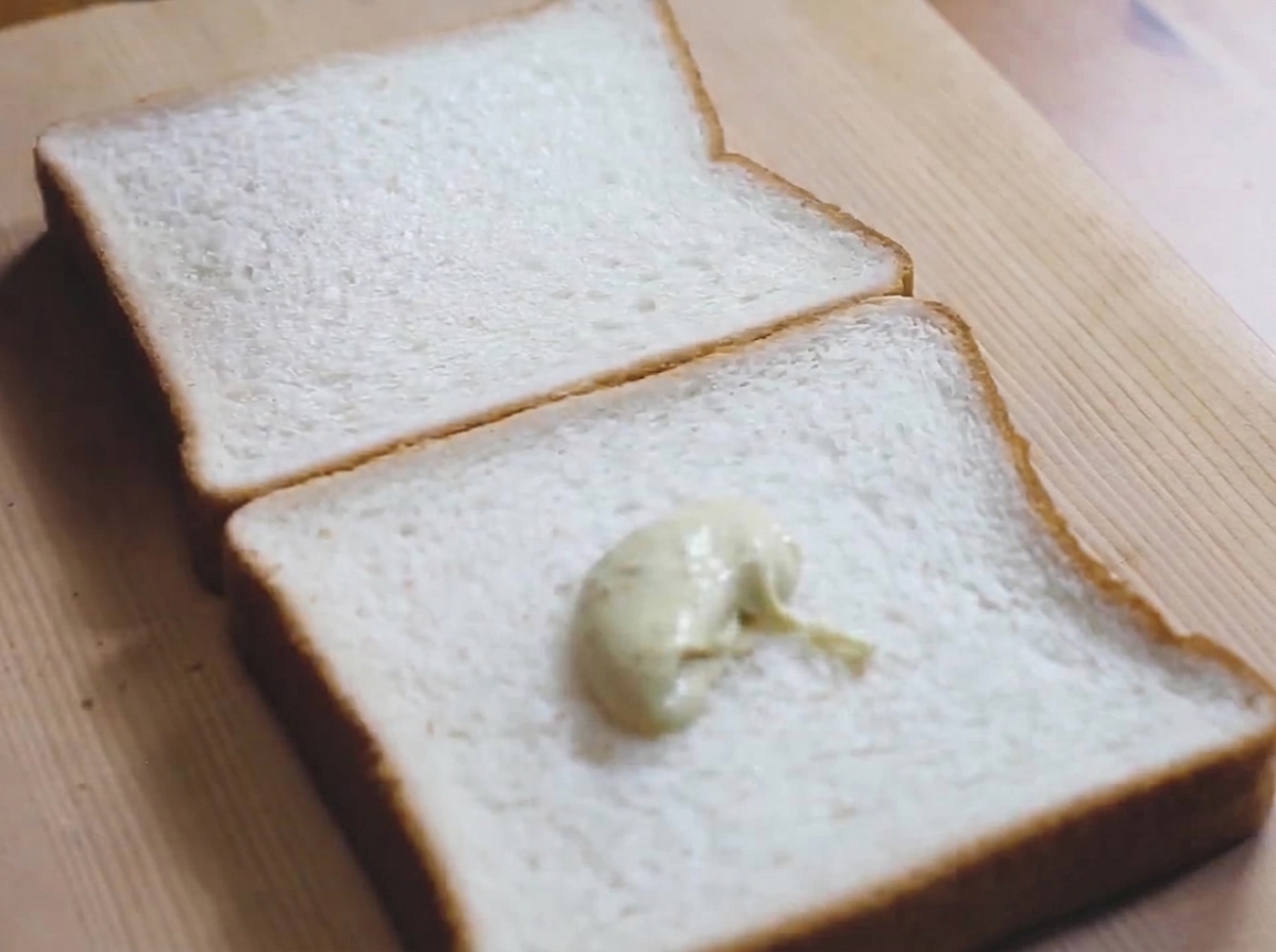 Una cucchiaiata di salsa maionese al wasabi verde chiaro stesa su una fetta di pane bianco su un tagliere di legno.