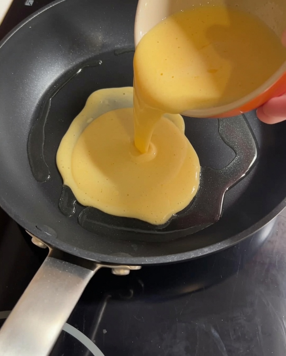 Miscela gialla di uova e latte versata in una padella calda, pronta per essere strapazzata.