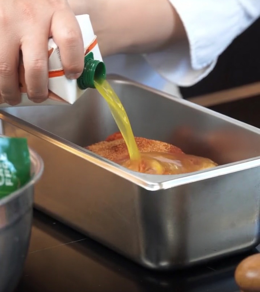 Succo darancia versato in una teglia da forno con la carne di maiale condita.