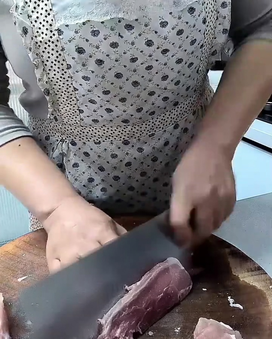 Una mannaia affilata che taglia un pezzo di lonza di maiale cruda su un tagliere di legno.