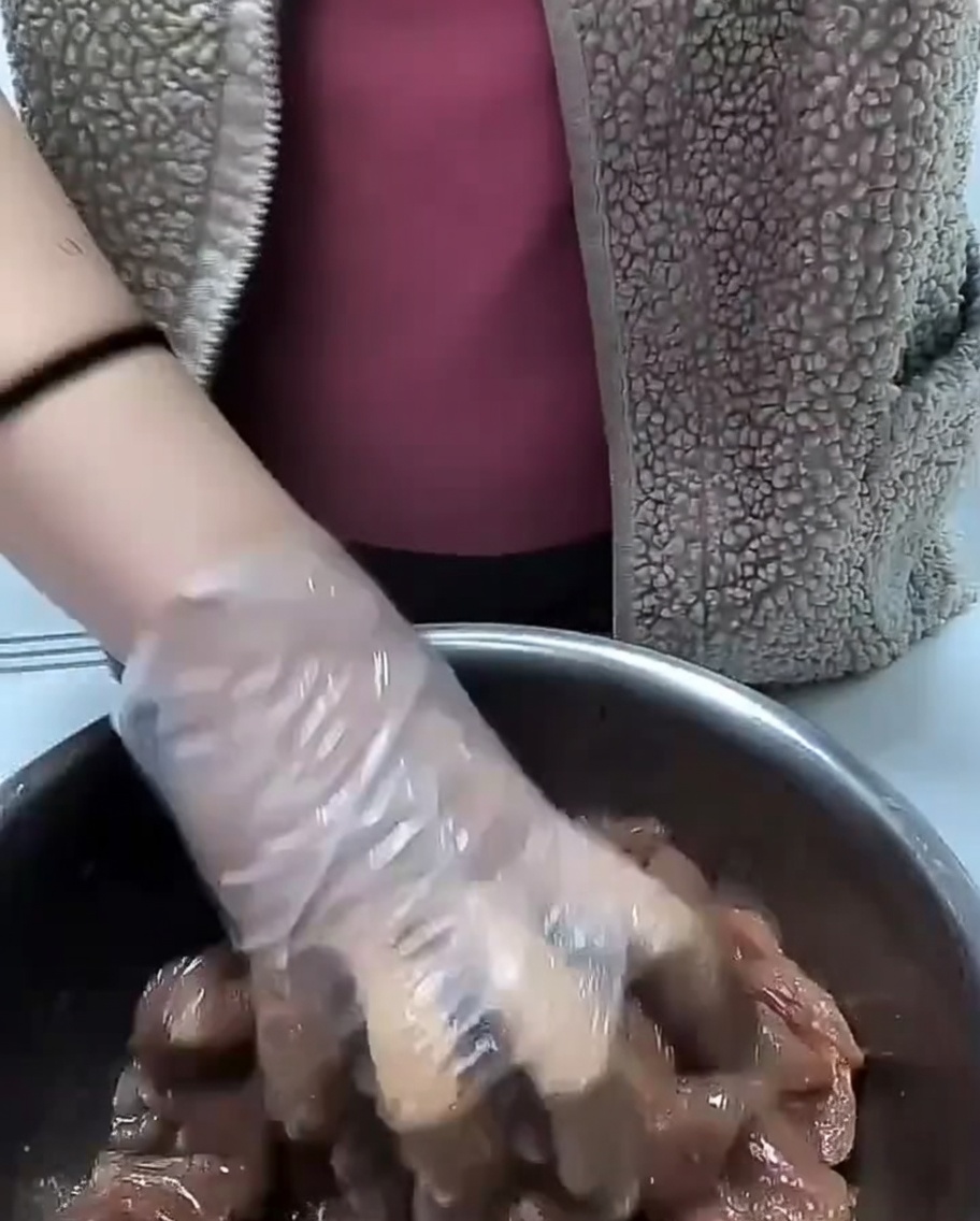 Olio da cucina versato sopra pezzi di maiale crudo condito in una ciotola di metallo.