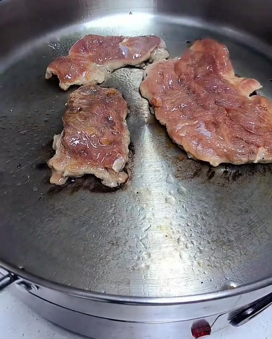 Braciole di maiale marinate che rosolano in una padella calda con una crosticina visibile sulla superficie.