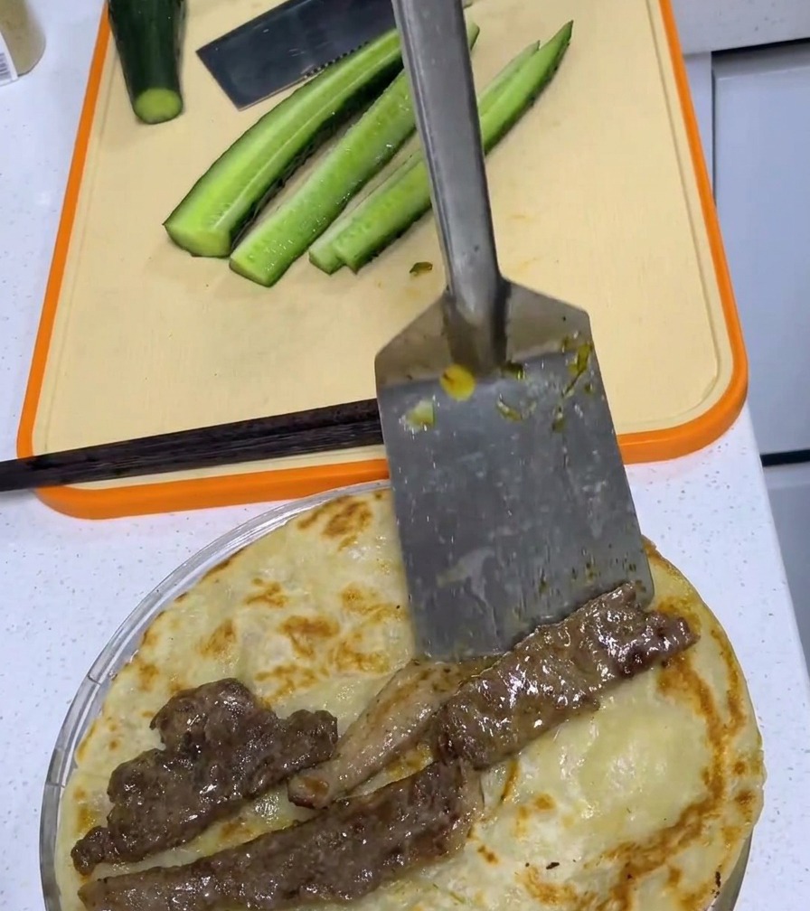 Una braciola di maiale fritta al centro di un pancake allo scalogno dorato su un tagliere.