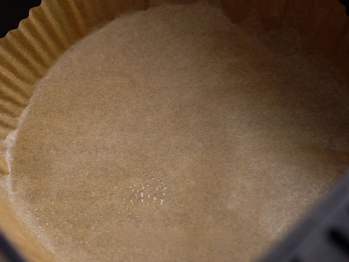 Patate tagliate a metà posizionate nel cestello della friggitrice ad aria rivestito di carta forno, pronte per essere condite.