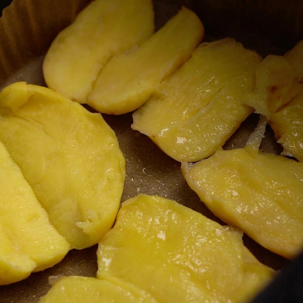Patate nel cestello della friggitrice ad aria coperte di olio, condite con sale grosso e una spolverata di semi di sesamo.
