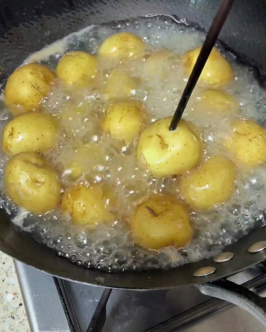 Patatine che sobbollono in acqua, testate con un bastoncino di legno.