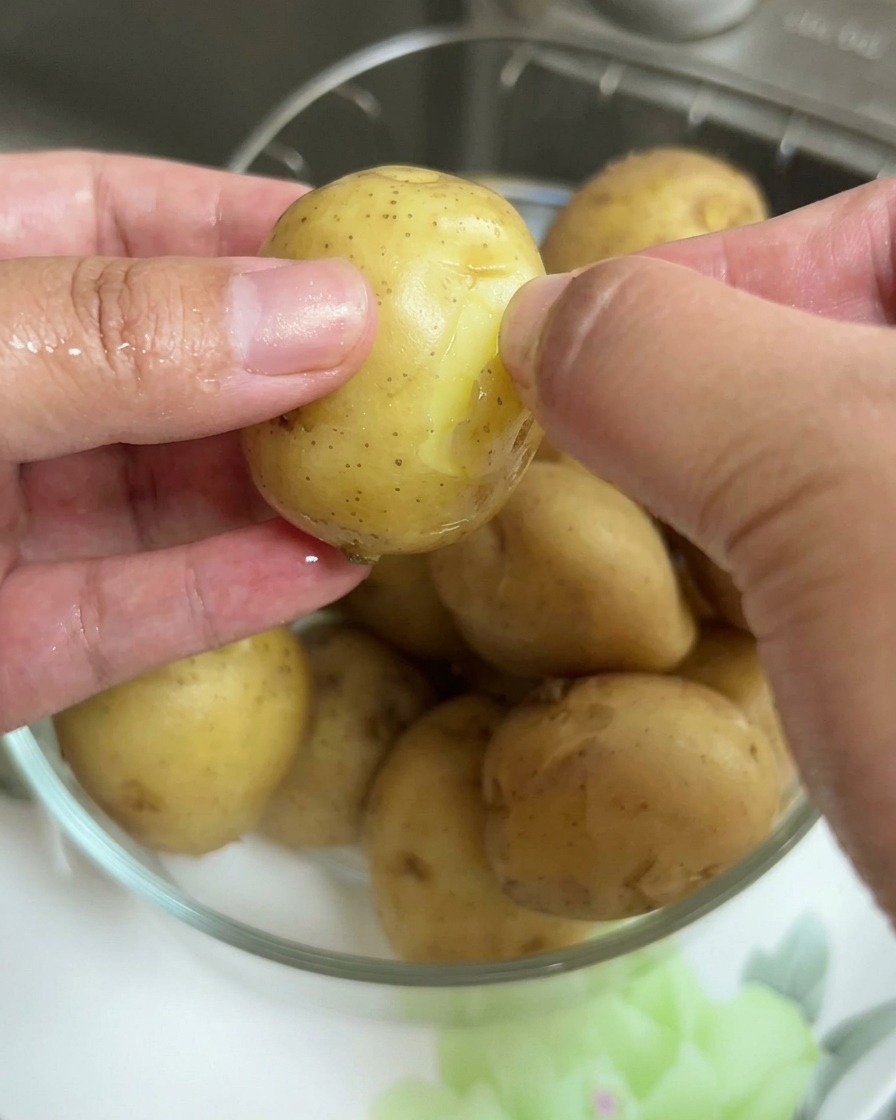 Mani che rimuovono la buccia sottile da una patatina bollita.