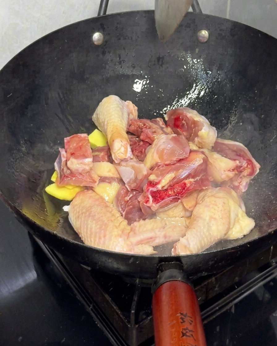 Pezzi di pollo fresco rosolati con fette di zenzero in un wok grande.