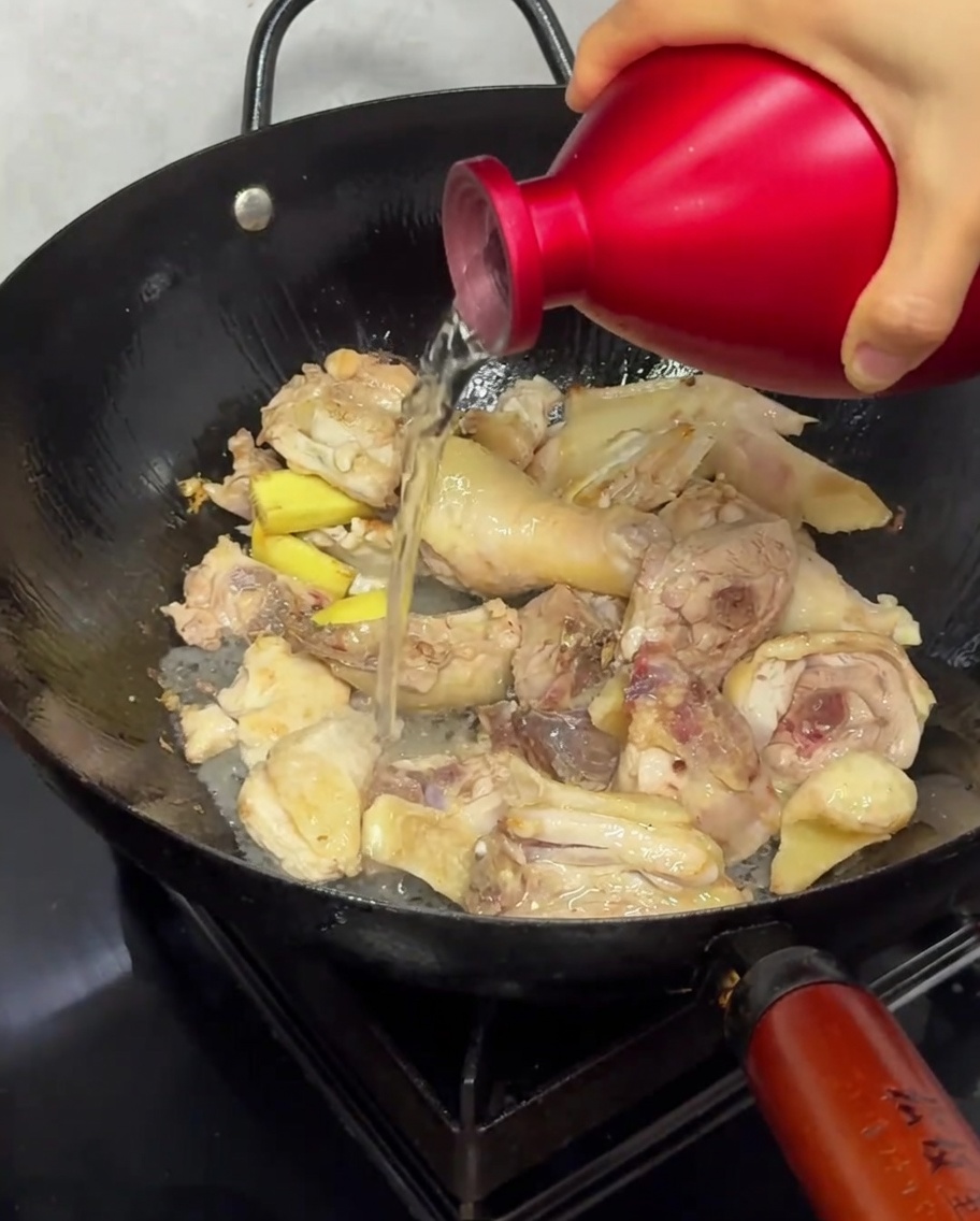 Vino di riso versato sopra i pezzi di pollo nel wok durante la rosolatura.