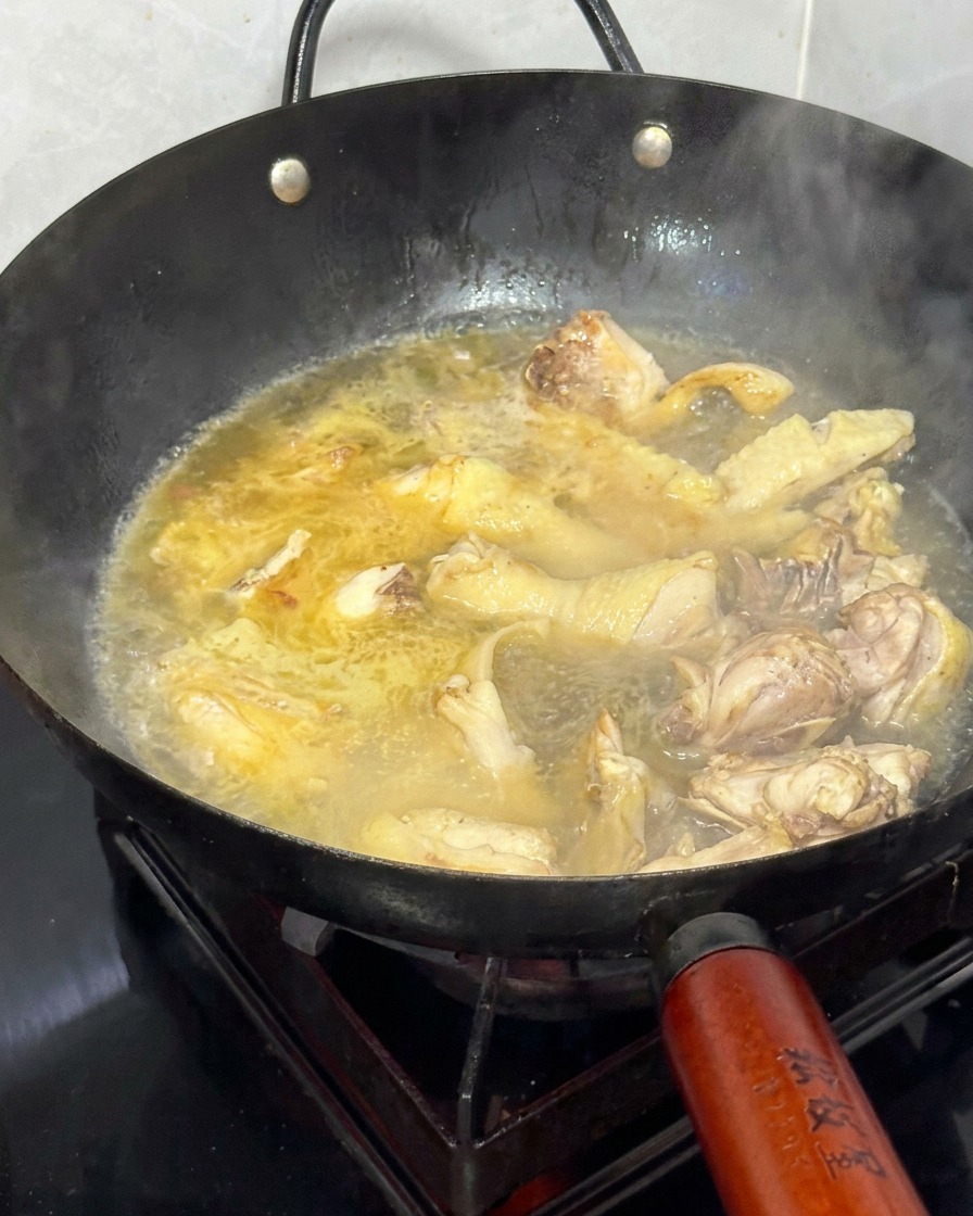Acqua calda versata in un wok riempito con pollo rosolato e zenzero.