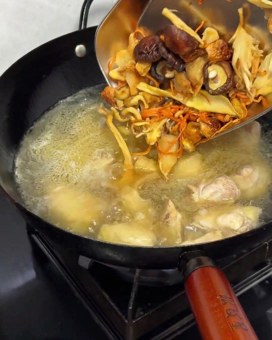 Funghi essiccati reidratati aggiunti in una pentola con pollo e brodo.