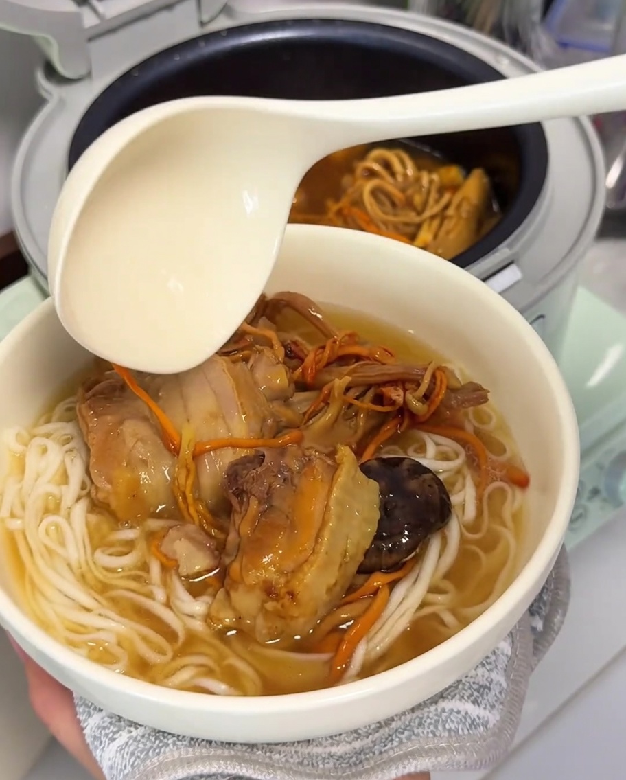 Un mestolo grande versa brodo di pollo e funghi caldo su una ciotola di noodle appena cotti.