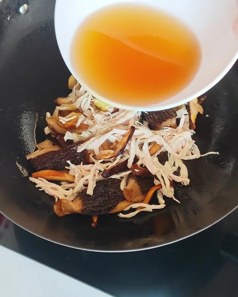 Il liquido di ammollo dei funghi versato nel wok con pollo e funghi.