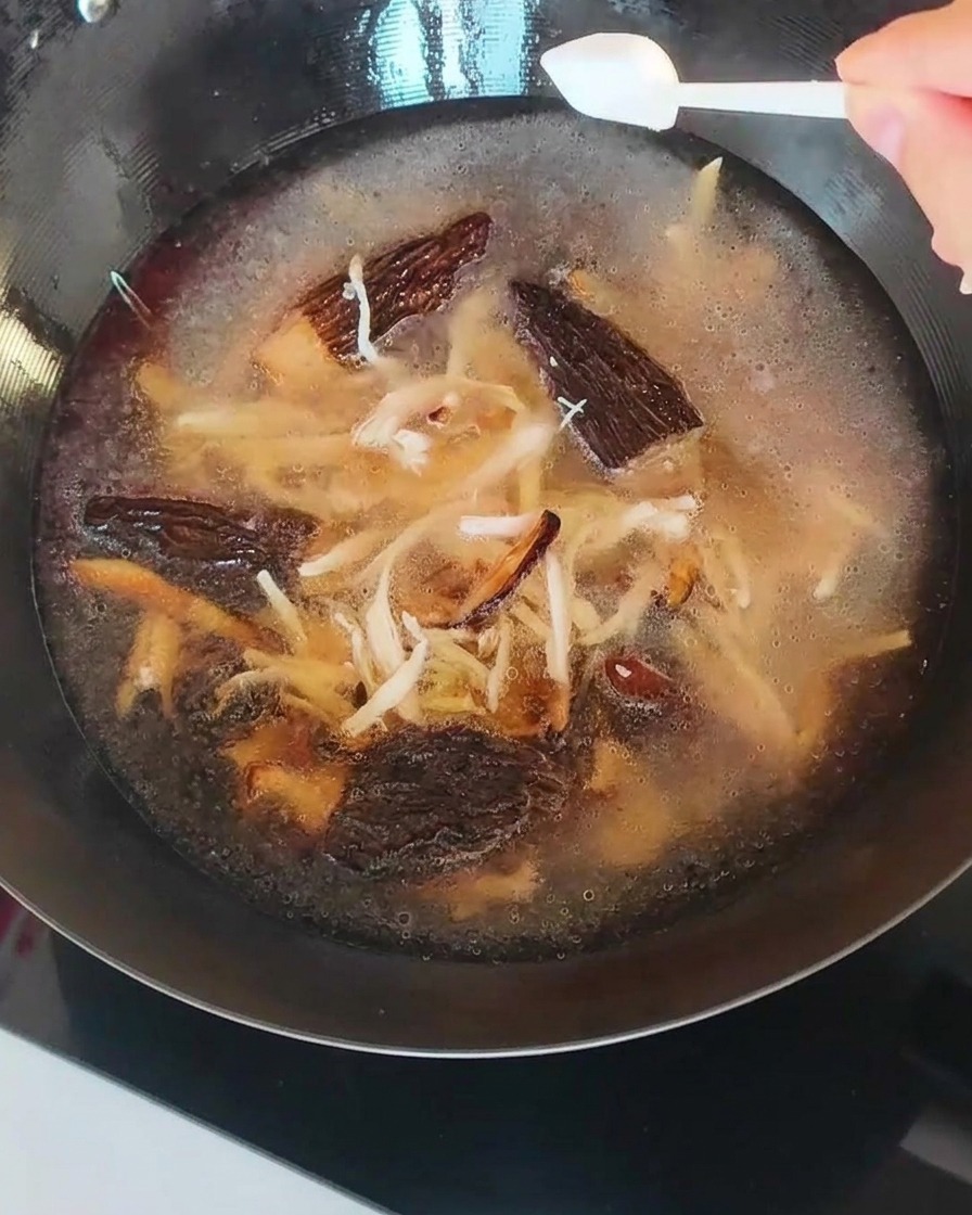 Il brodo nel wok, con funghi e pollo sfilacciato, mentre viene salato.
