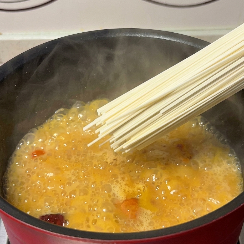 Una manciata di noodles secchi immersi in un tegame di brodo dorato.