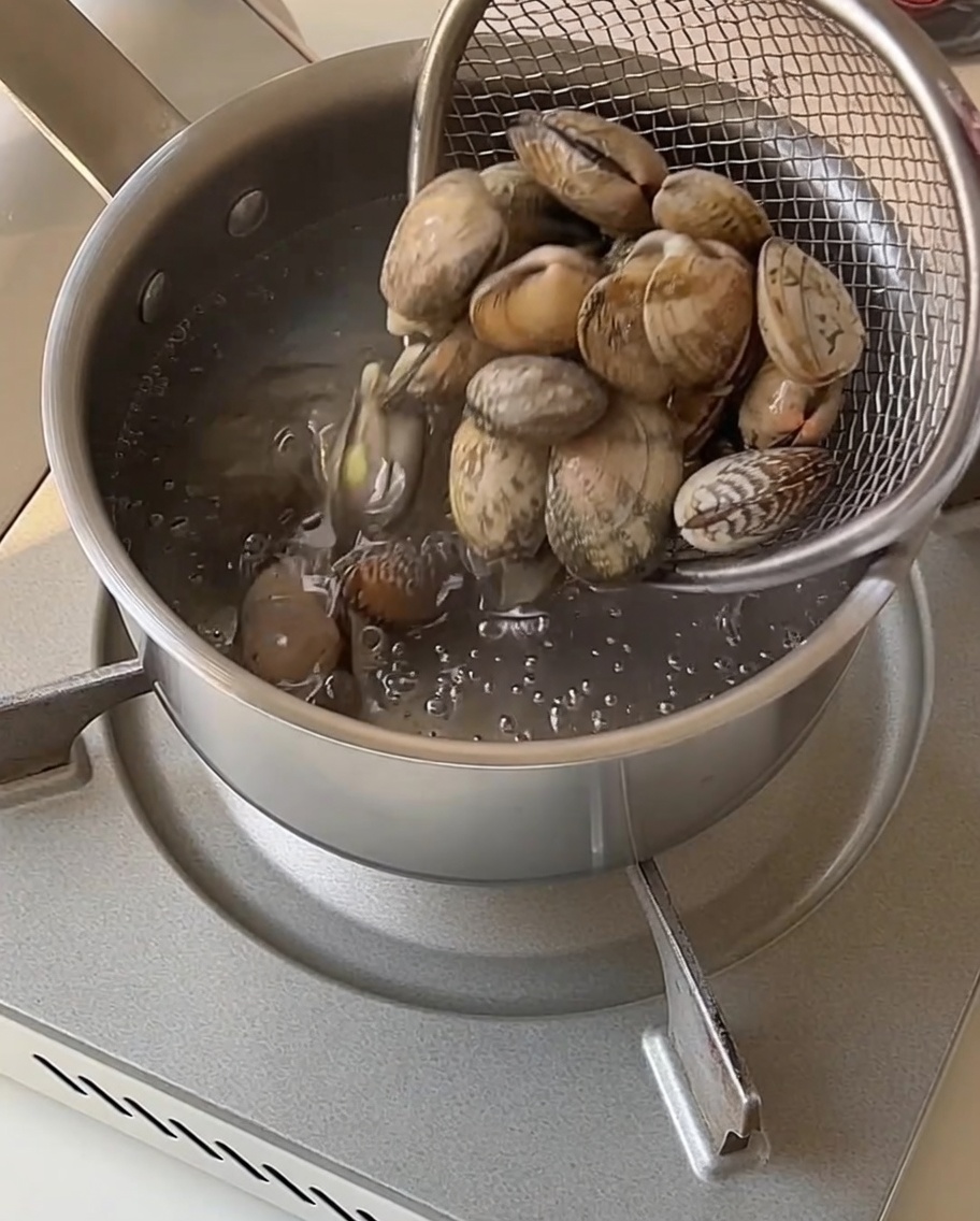 Vongole sollevate in un colino a rete da una pentola di acqua bollente.
